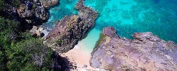 An aerial view of a tropical beach surrounded by rocks and trees.