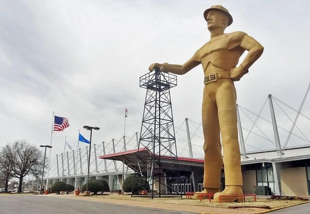 A statue of a man in a hard hat is standing in front of a building.