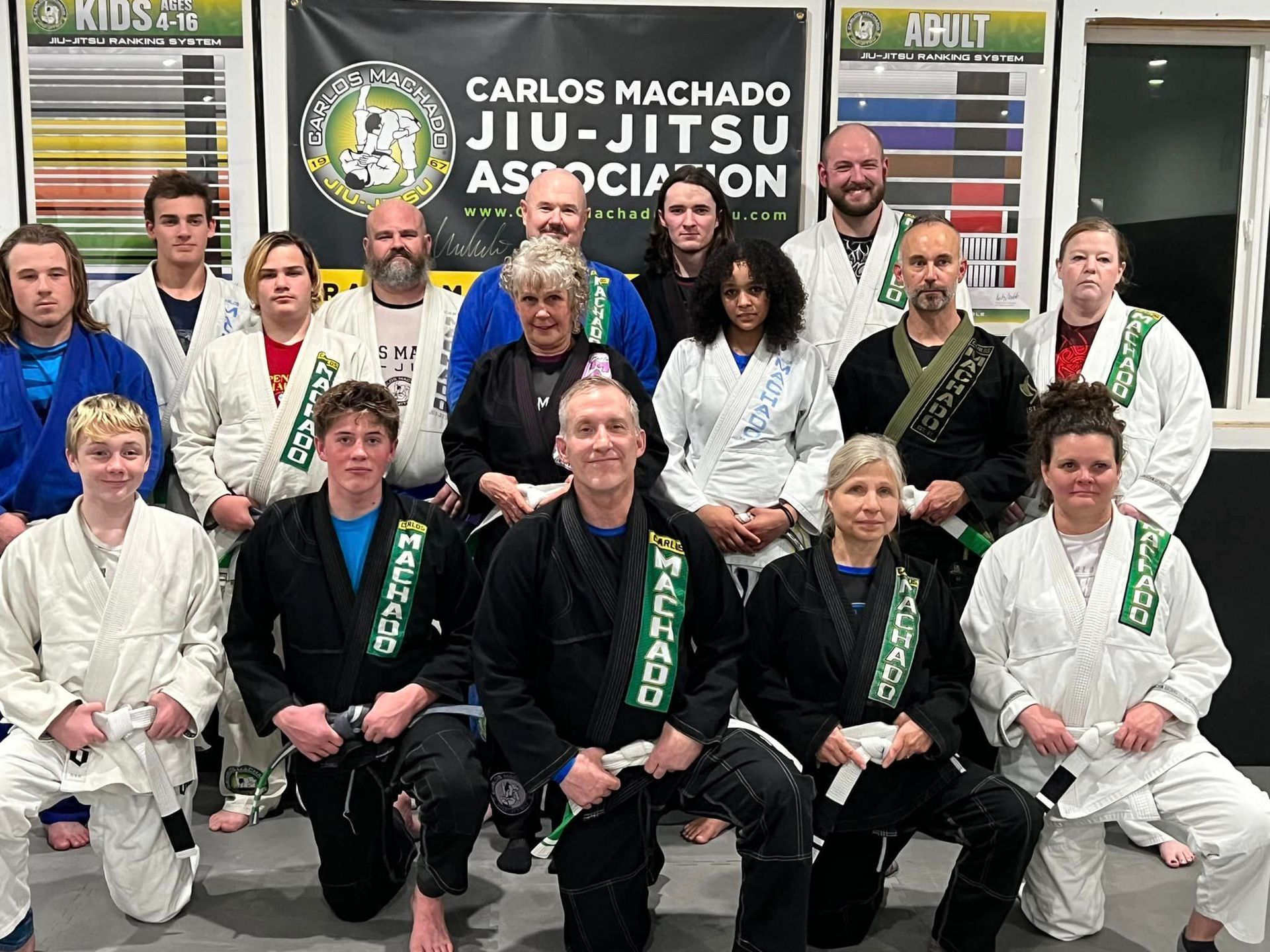 A group of people posing for a picture in front of a sign that says carlos machado jiu-jitsu association