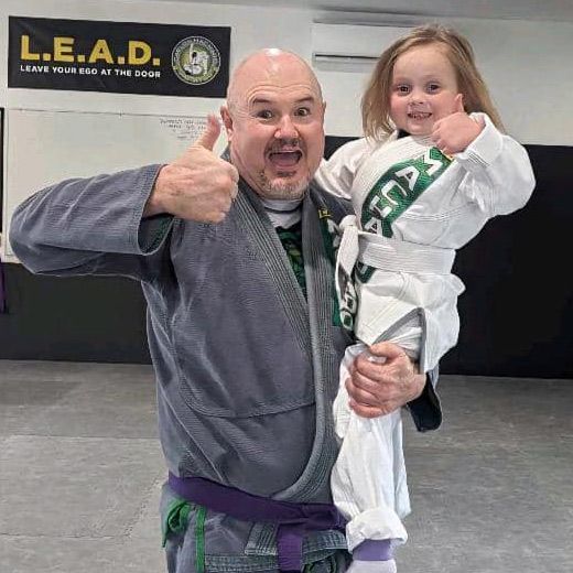 A man is holding a little girl in front of a sign that says l.e.a.d.