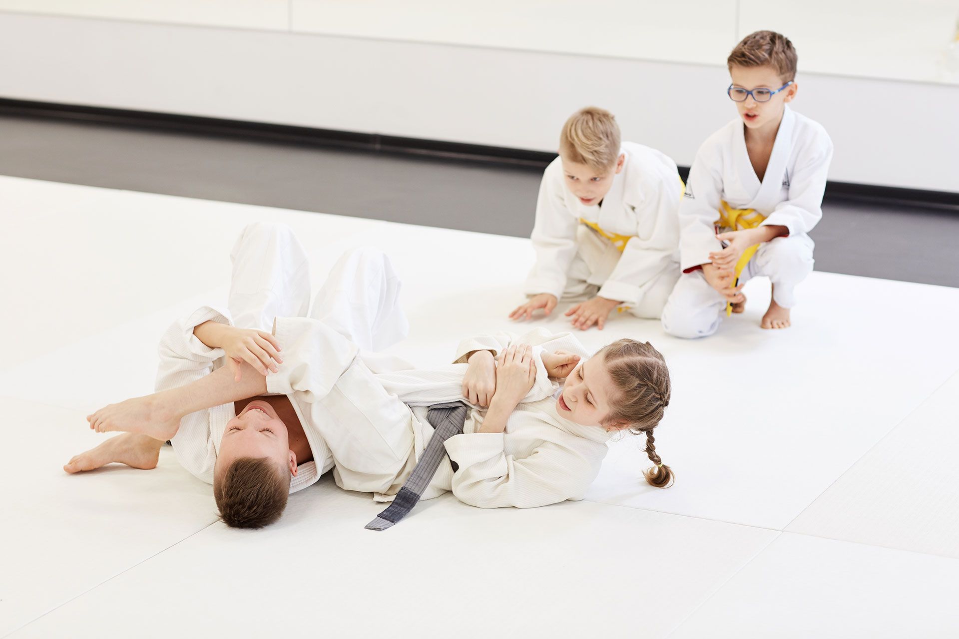 A group of young children are practicing judo in a gym.