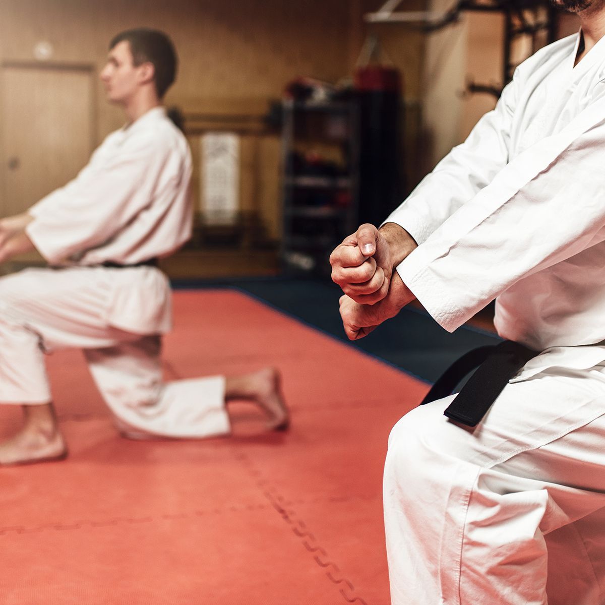 Two men in karate uniforms are kneeling on a mat in a gym.