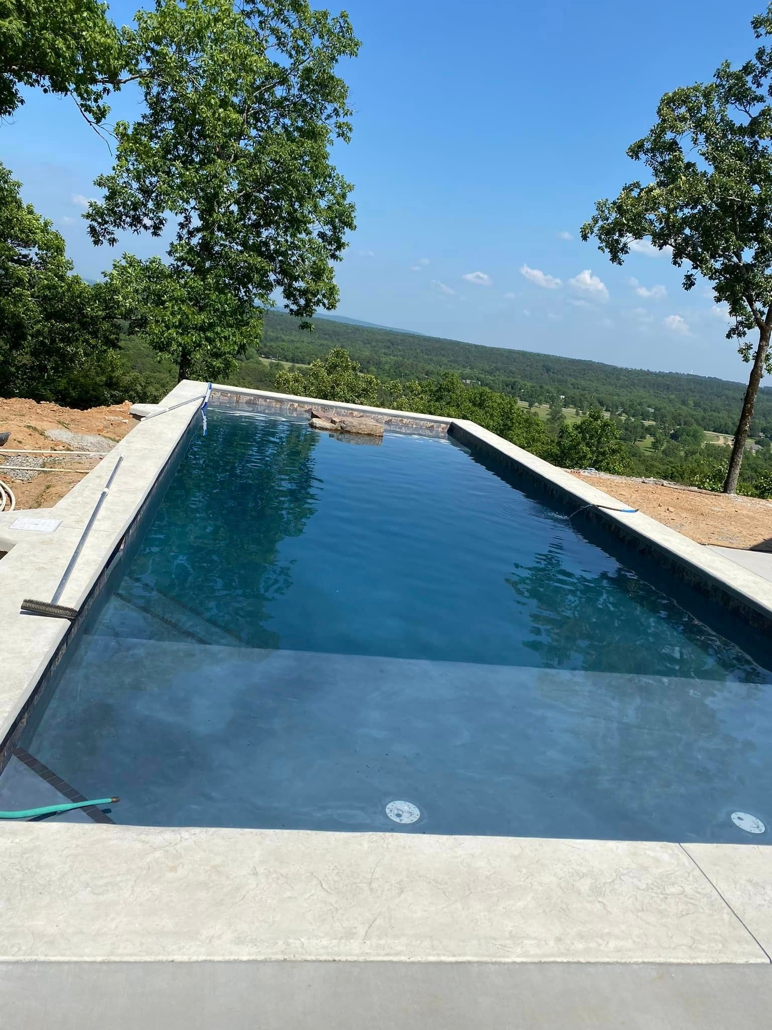 A large swimming pool is surrounded by trees on a hillside.