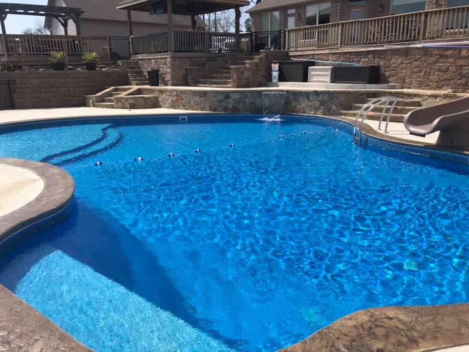 A large swimming pool with a slide in the backyard of a house.