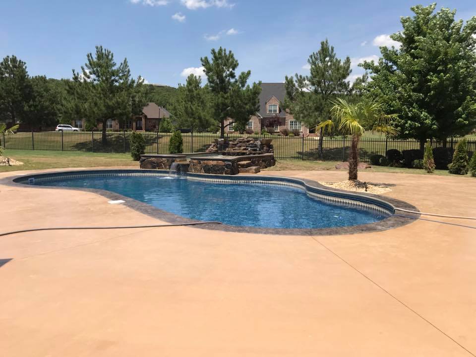 A large swimming pool with a waterfall in the backyard of a house.