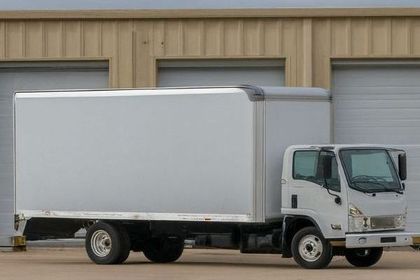 A white moving truck is parked in front of a building.