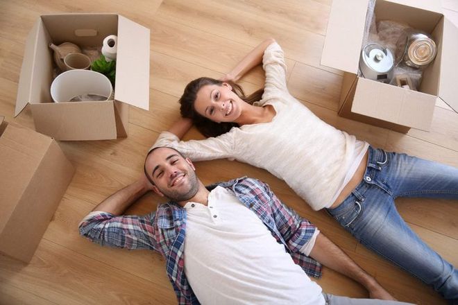 A man and a woman are laying on the floor next to moving boxes.