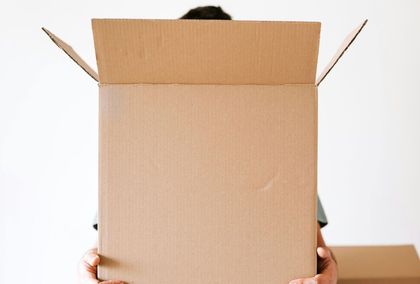 A person is holding a cardboard box in front of their face.