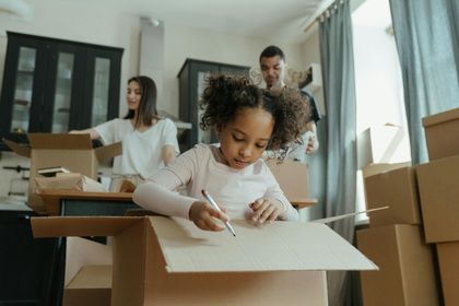 A little girl is sitting in a cardboard box writing on it.