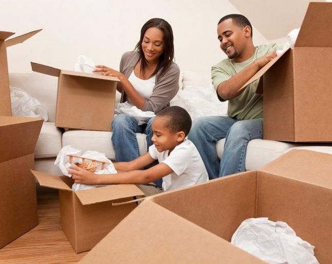 A family is sitting on a couch surrounded by cardboard boxes