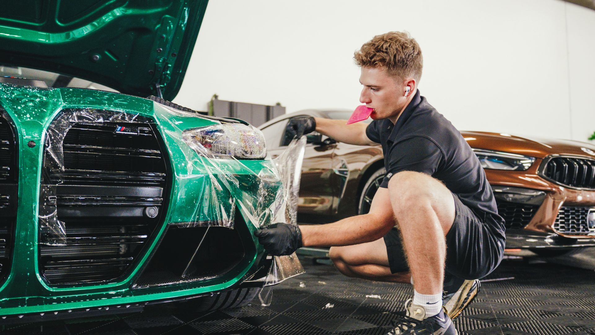 A man is covering the front of a green car with plastic wrap.
