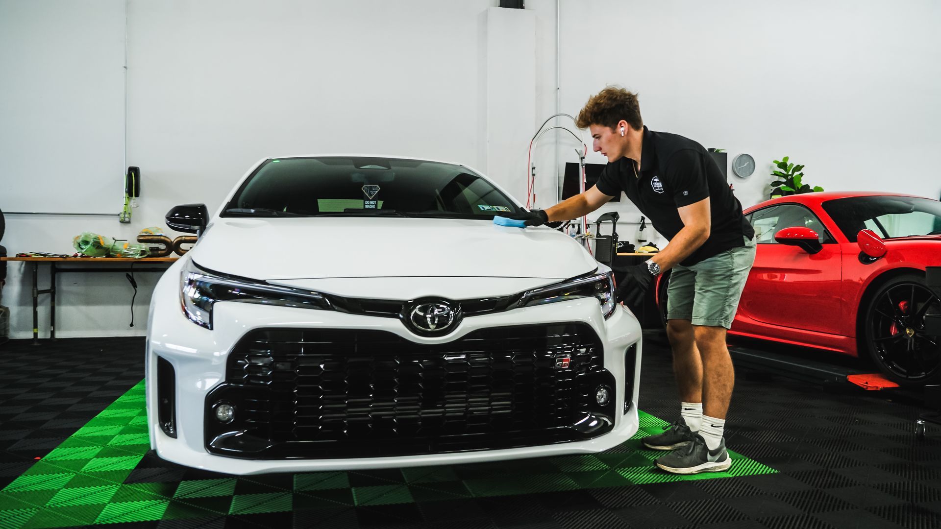 A man is cleaning a white car in a garage.