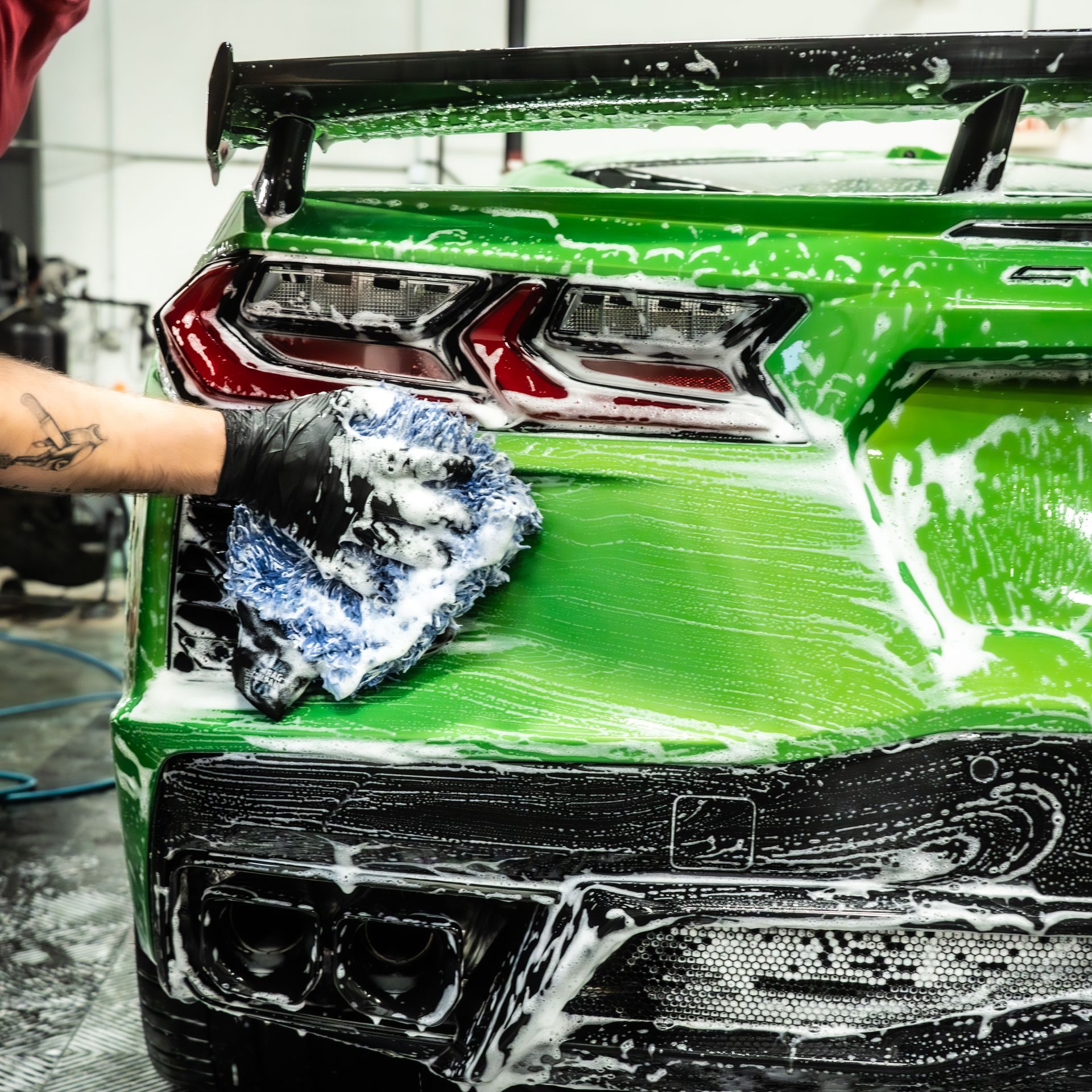 Green sports car being washed with soapy sponge.