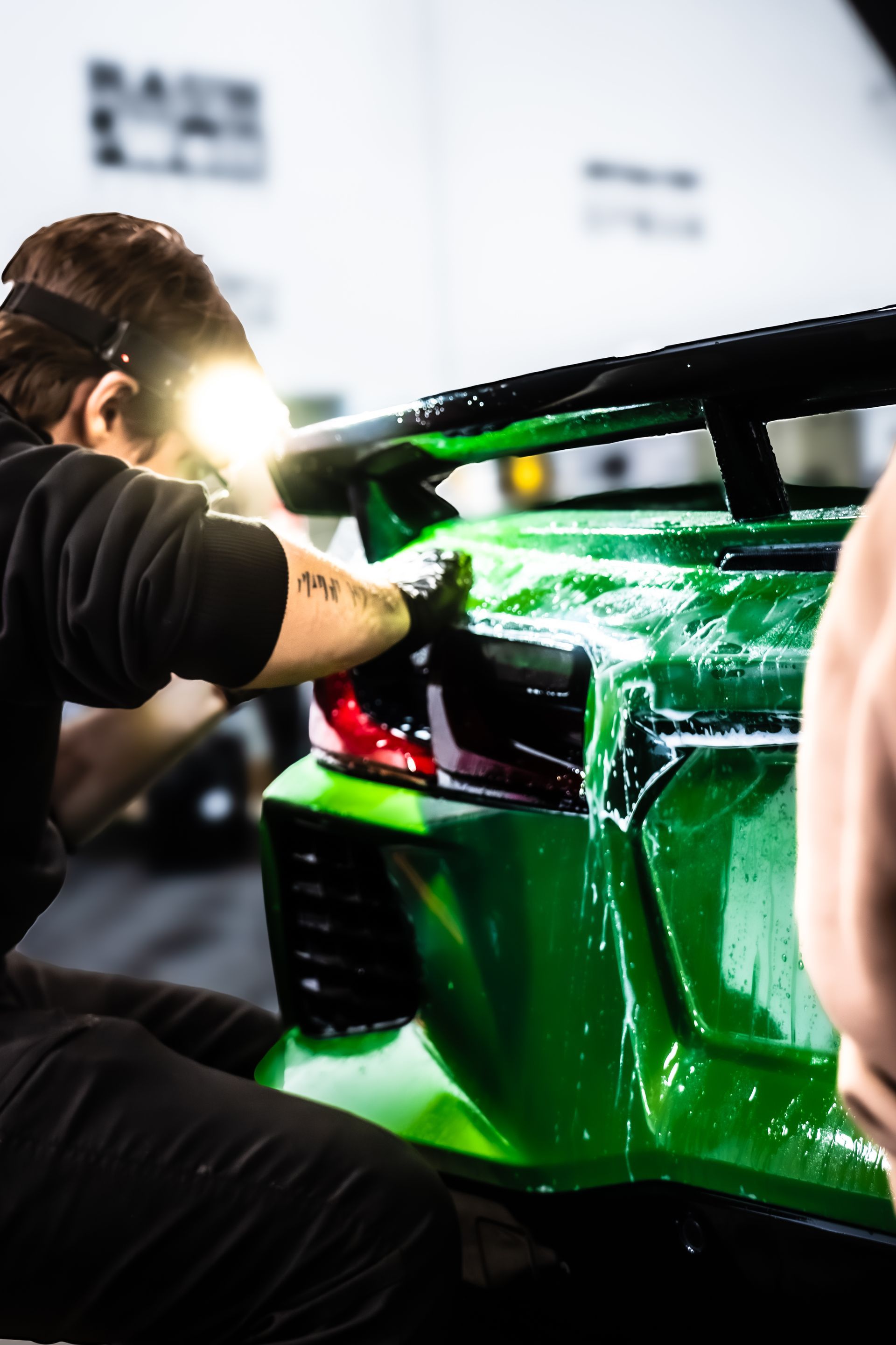 Person applying film to a green sports car's taillight. Focus on detailed work and the car's paint.