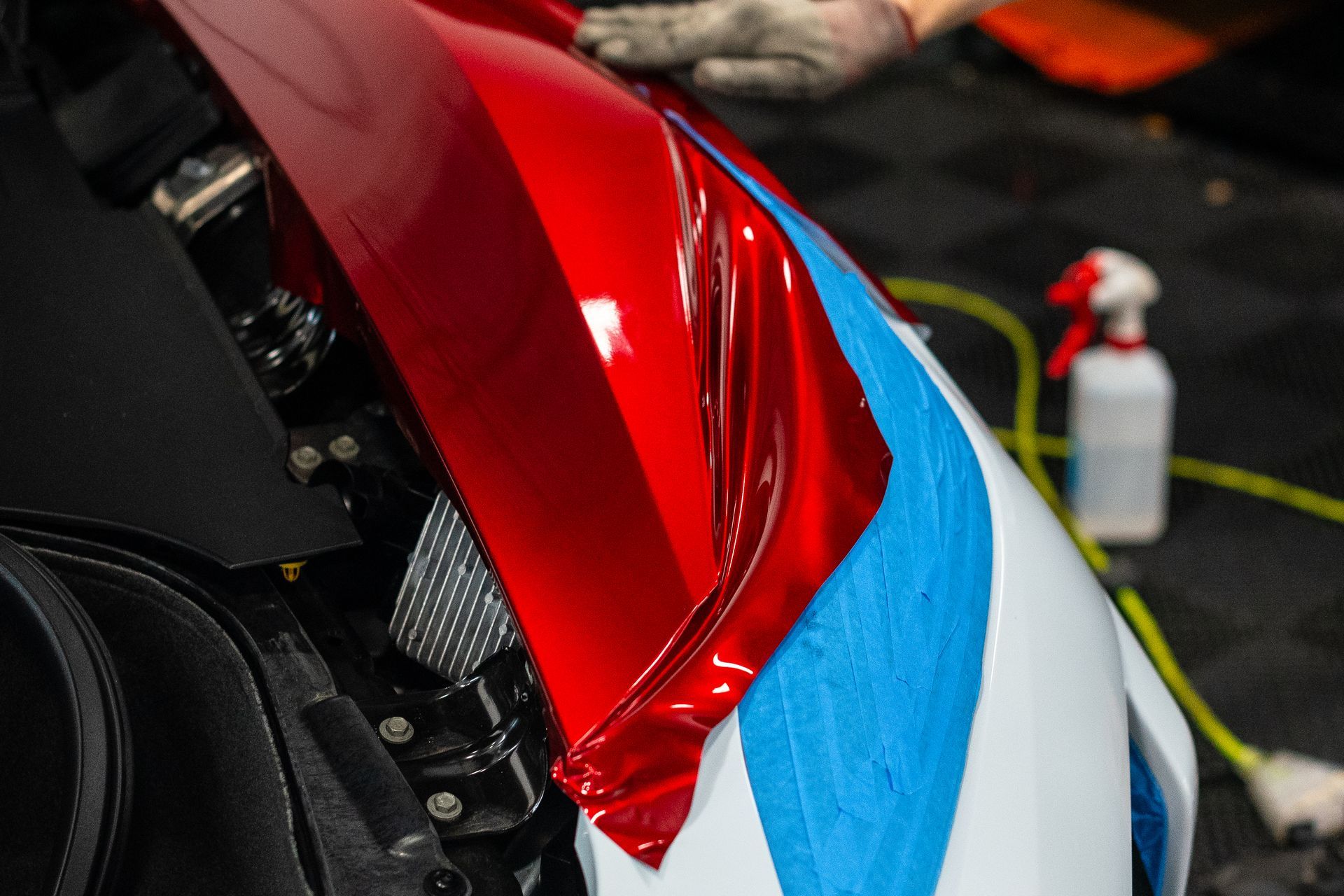 A person is wrapping a red car with blue tape.