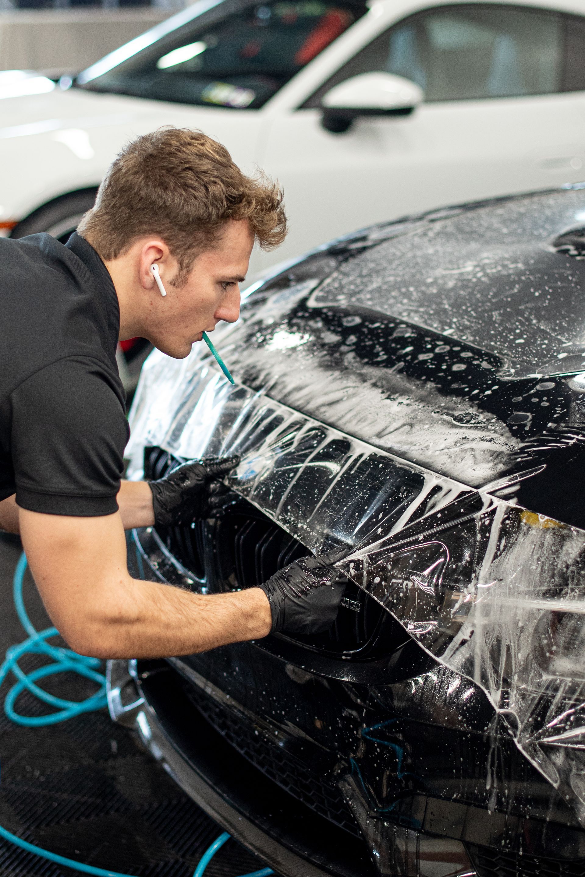 A man is washing a black car with a hose.