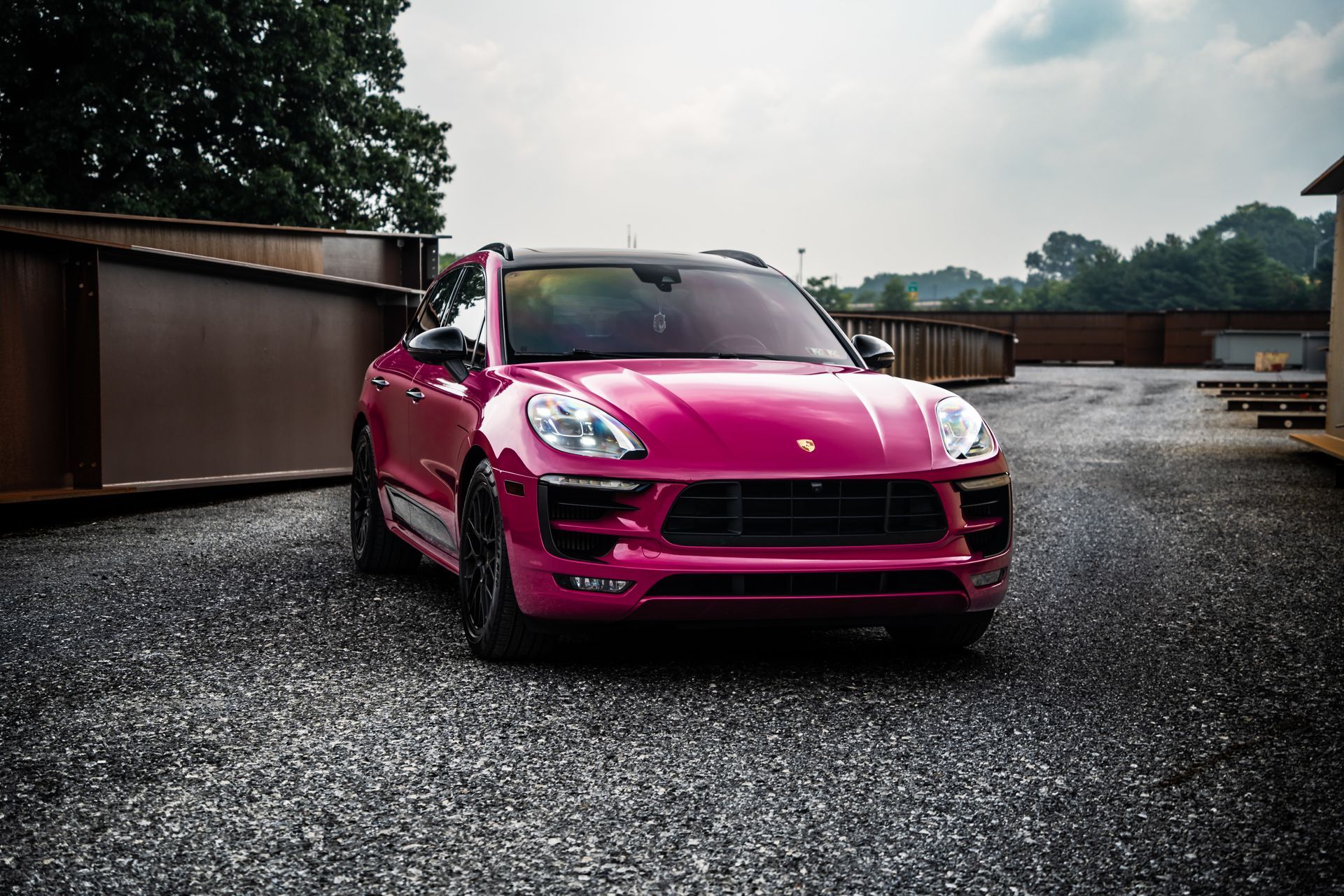 A pink porsche macan turbo is parked in a gravel lot.