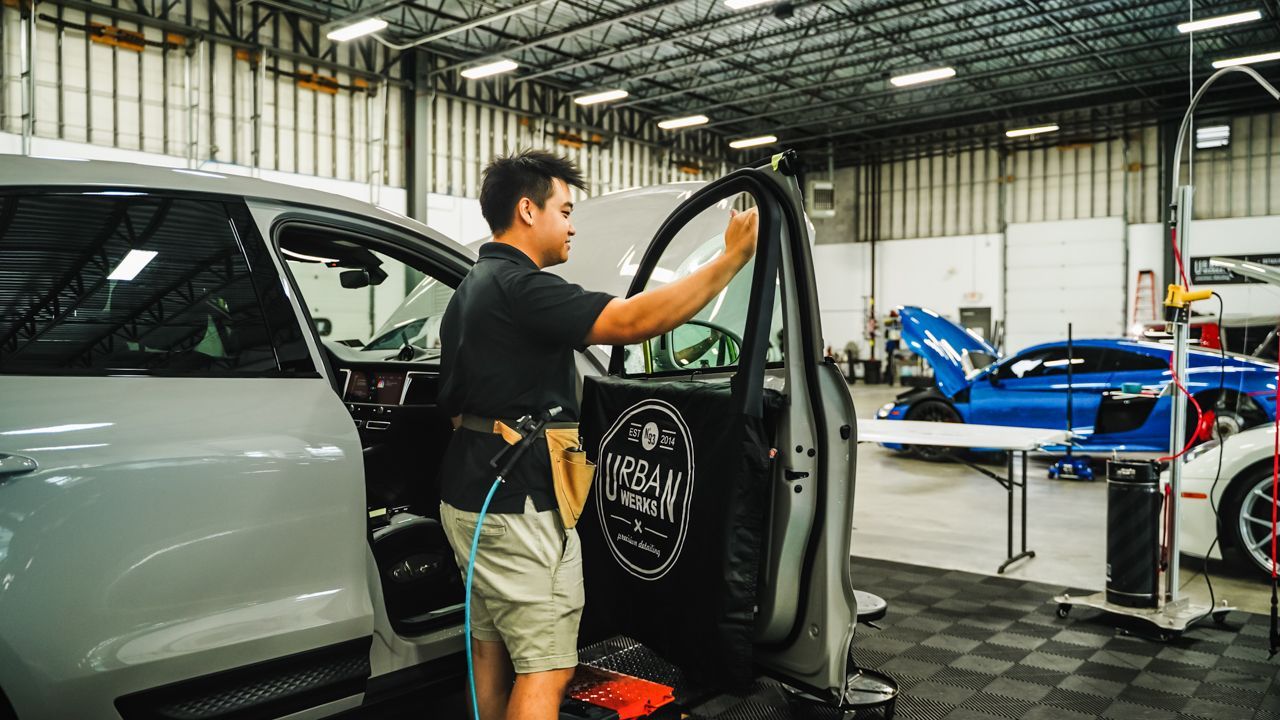 A man is cleaning the windows of a car in a garage.