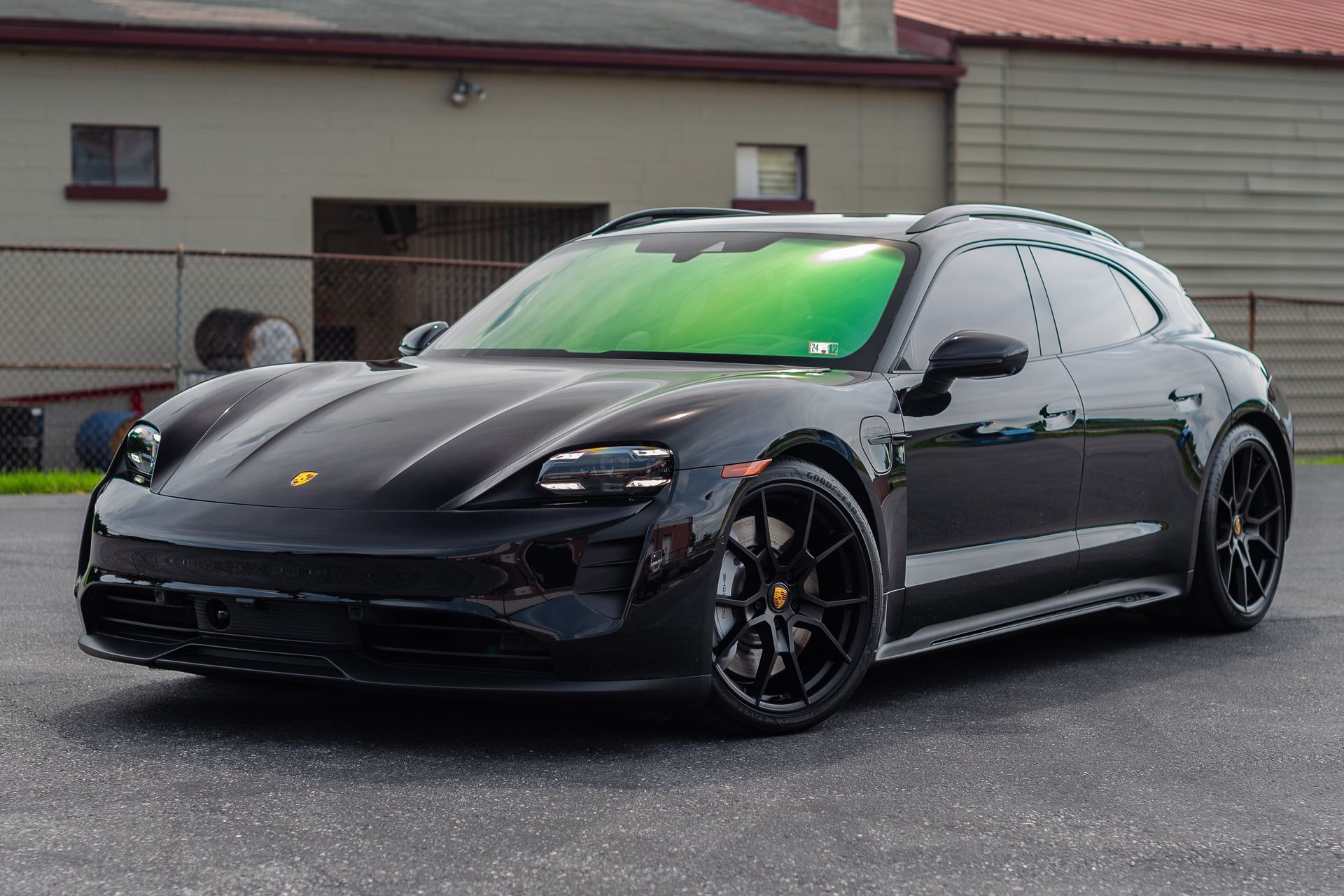 A black porsche taycan turbo s is parked in a parking lot in front of a building.