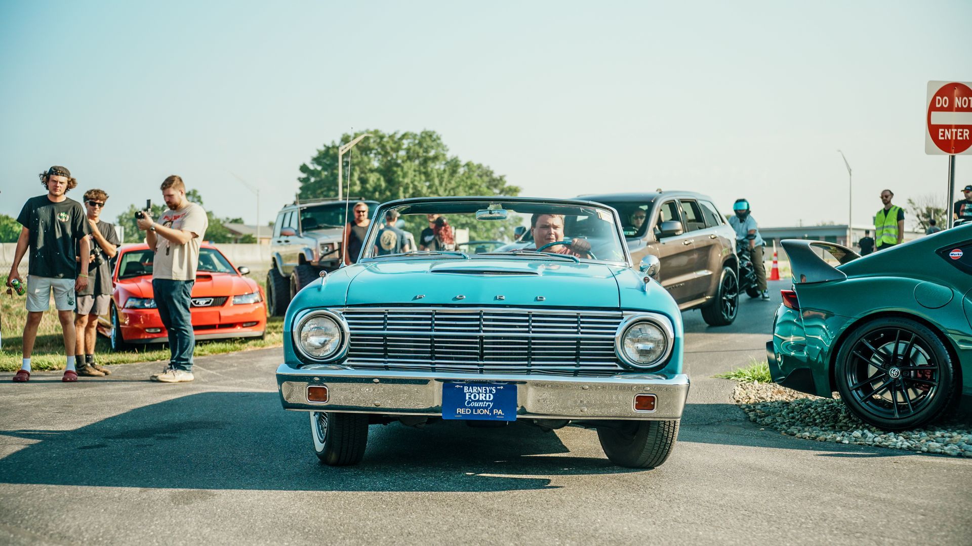 A group of people are standing around a blue car in a parking lot.