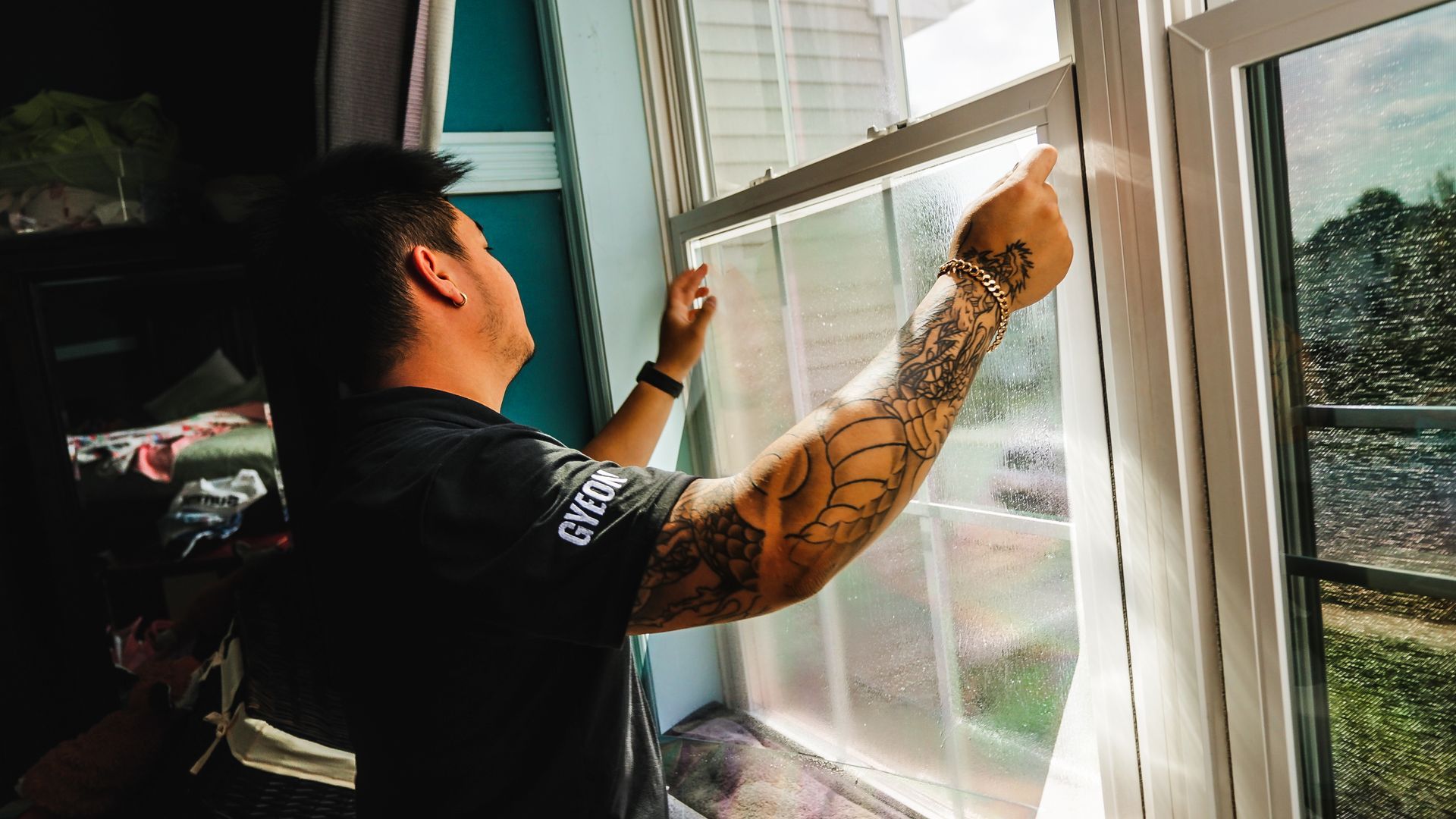 A man with tattoos is installing window film on a window.