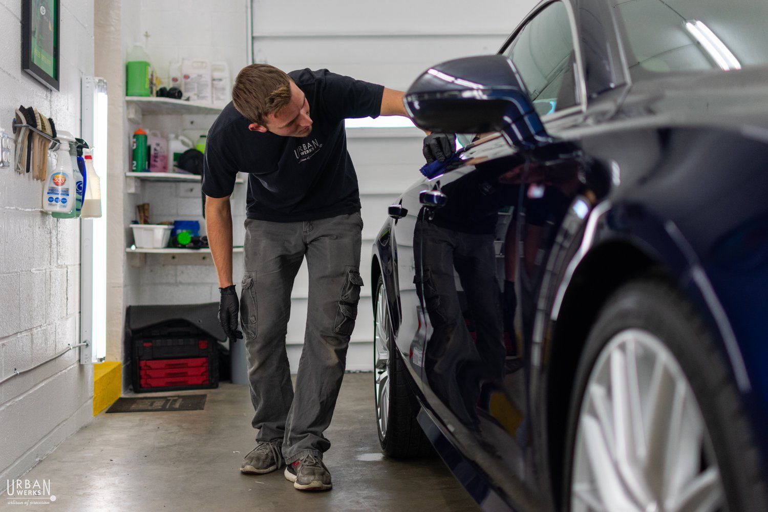 A man is standing next to a blue car in a garage.