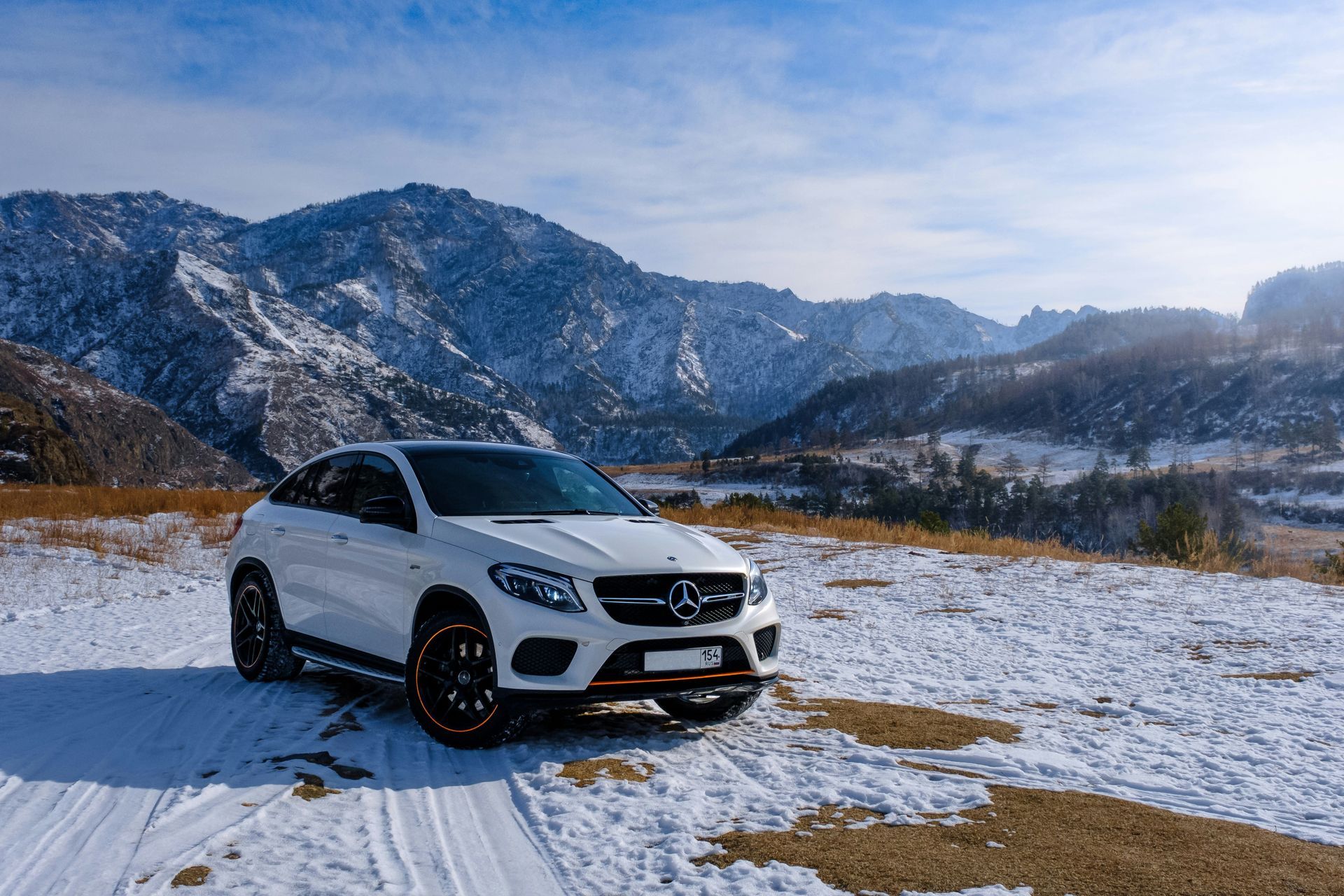 A white car is parked in the snow in front of a mountain.