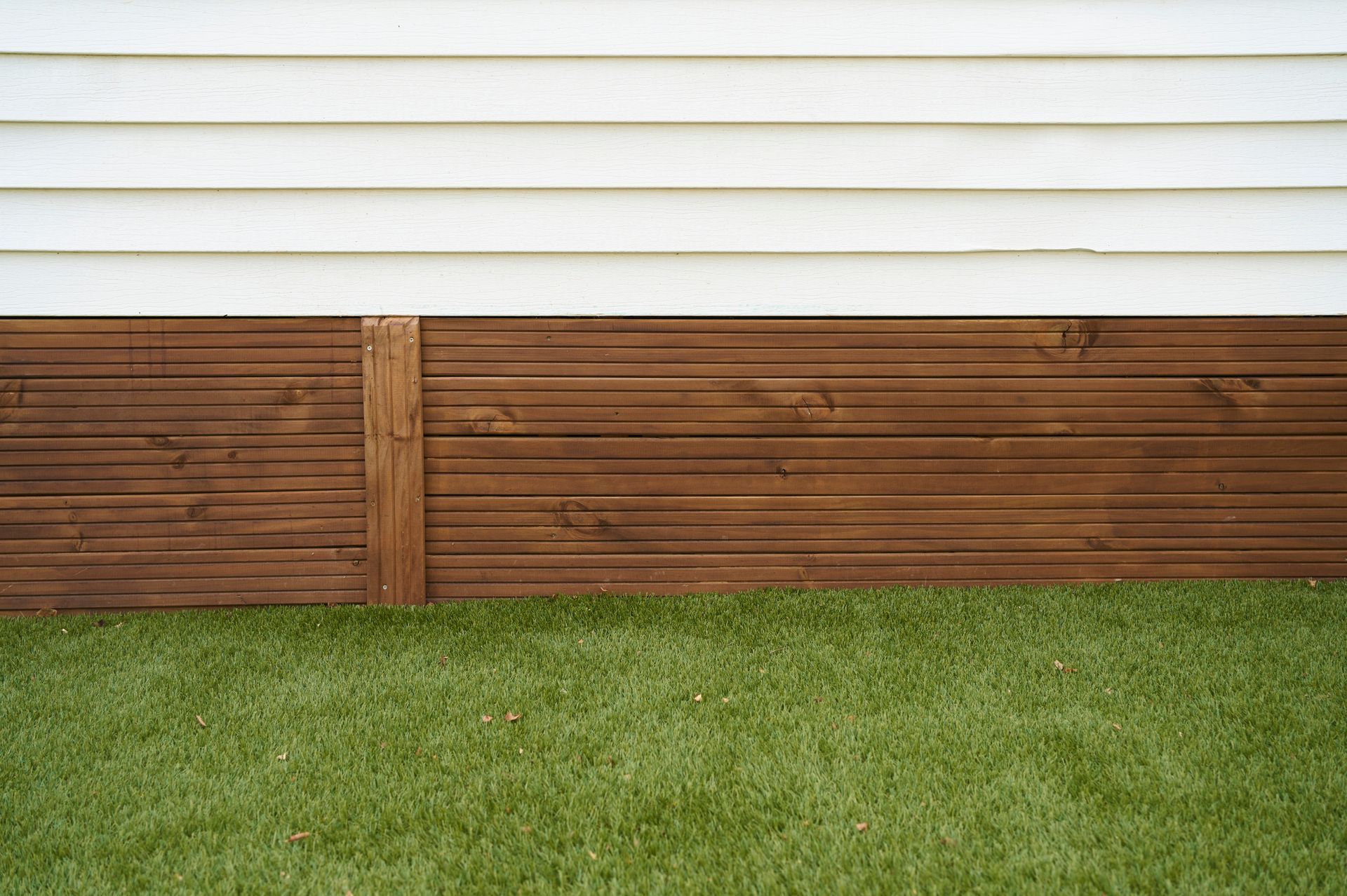 Brown wooden siding below white clapboard siding, over green grass.