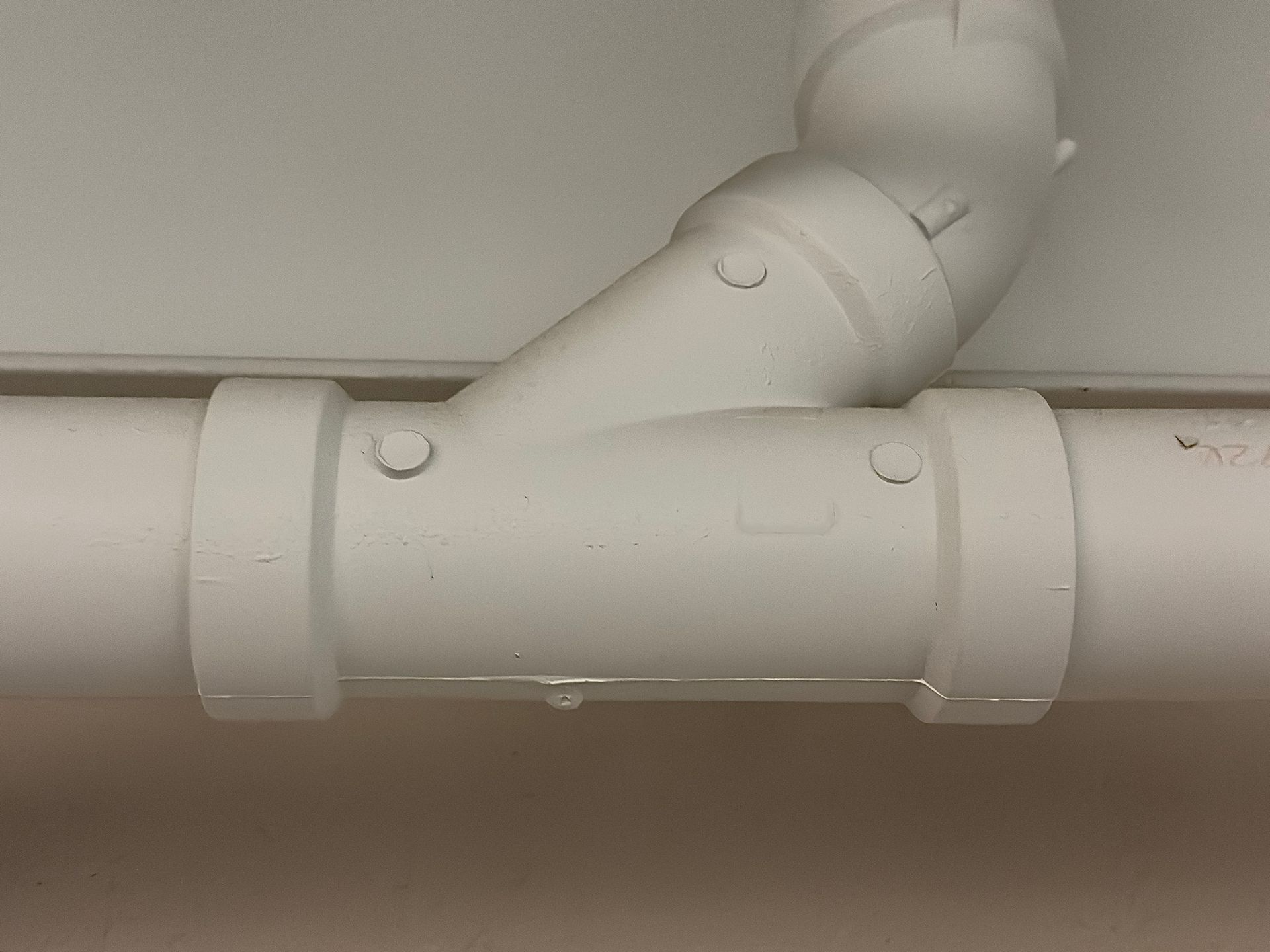 White painted plumbing pipes with a Y-joint connecting two sections to an angled pipe.