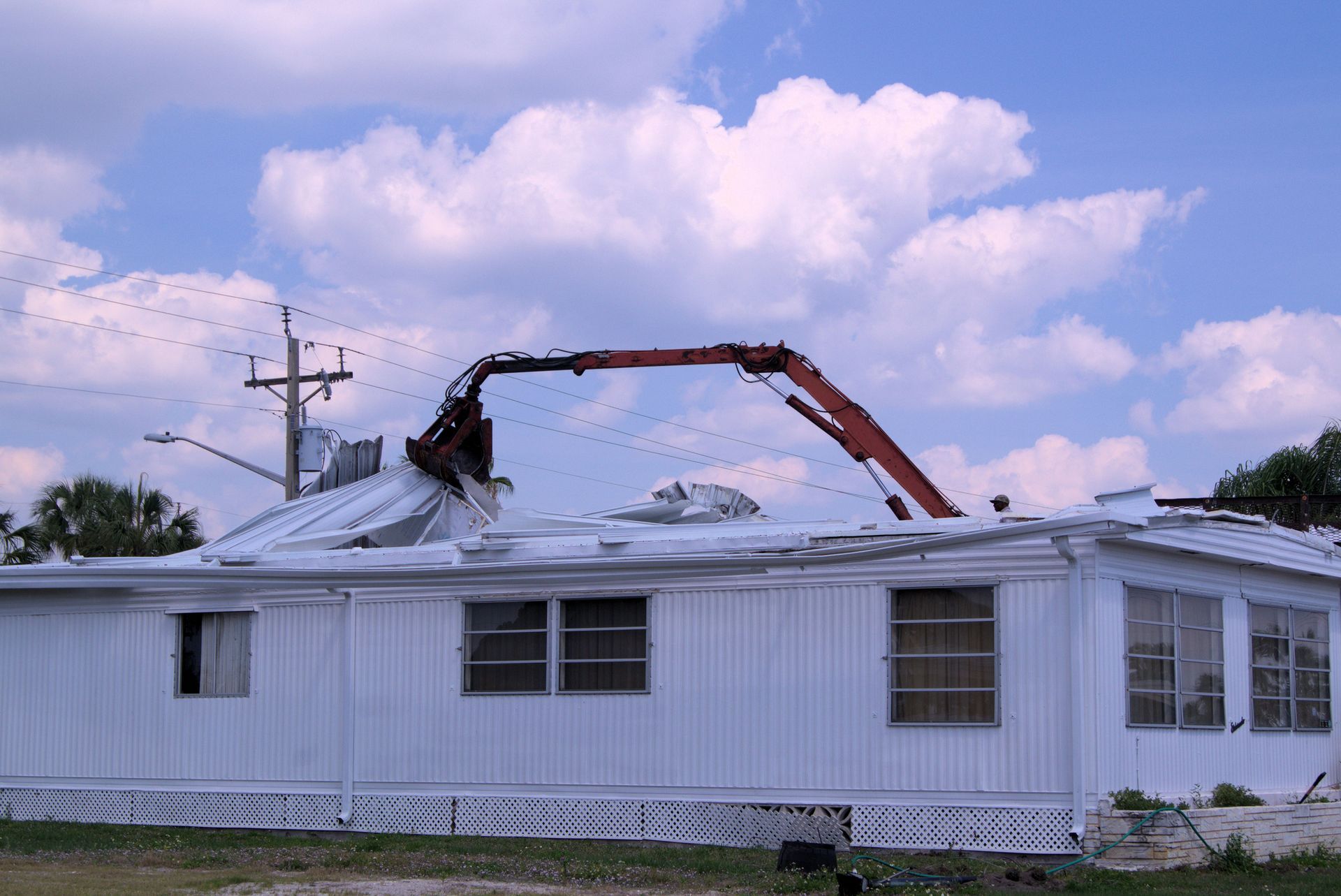 A mobile home being demolished by a large excavator on a sunny day.