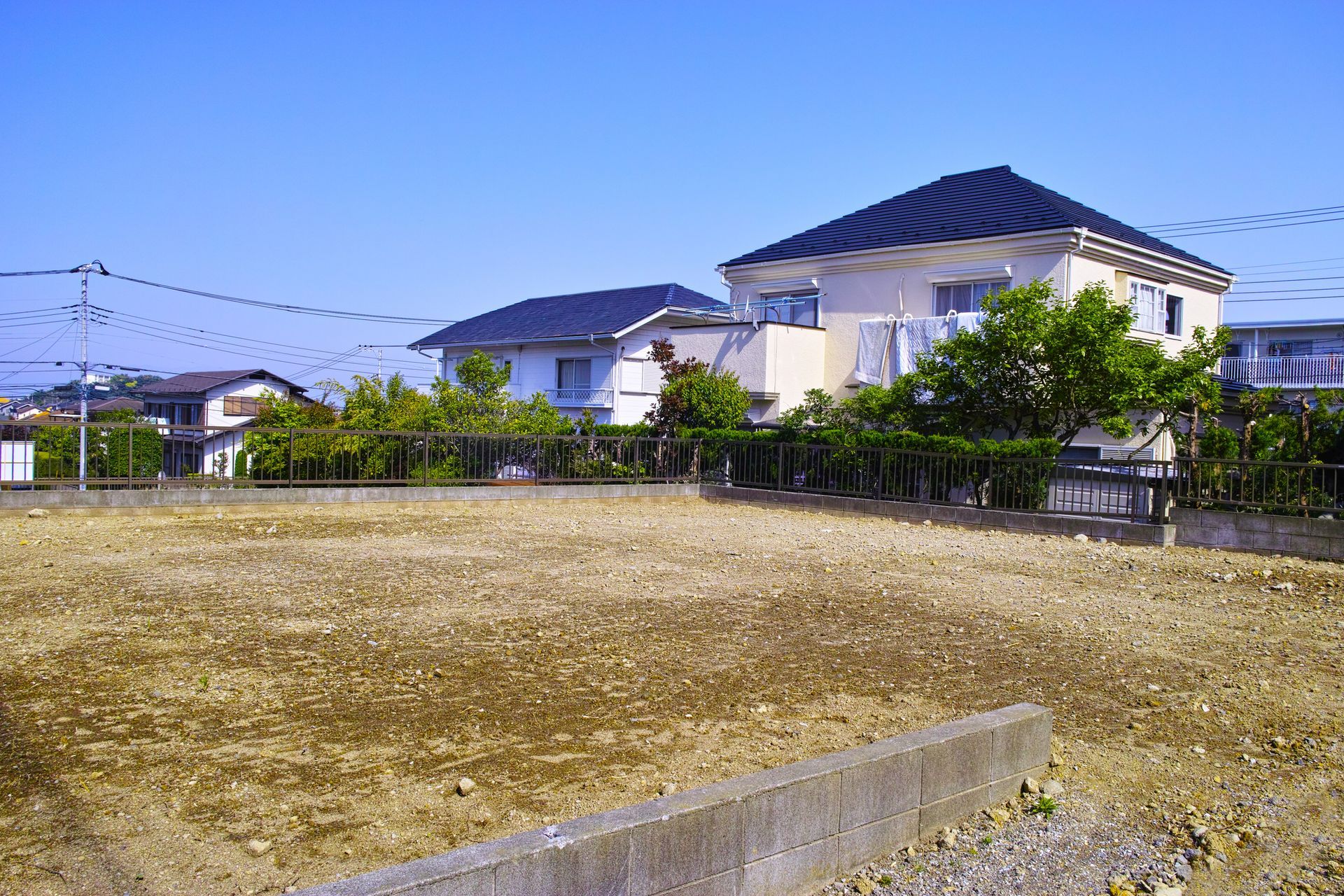 Cleared lot with houses in the background under a blue sky.