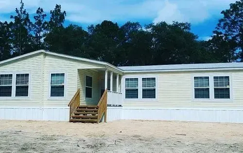 Light yellow manufactured home with a porch and stairs. Trees in the background.