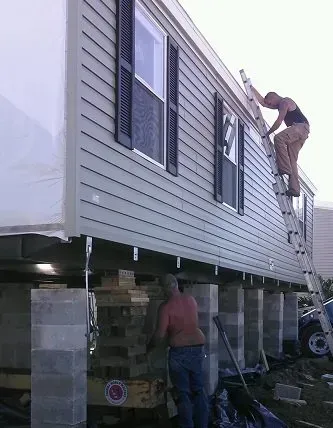 Men working to level a mobile home, using jacks and a ladder.