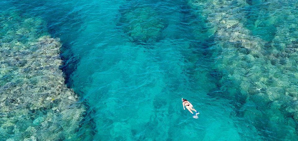 A photo taken from above, of a young woman swimming in bright blue waters, taken from one of our ads for Auberge Resorts Collection.