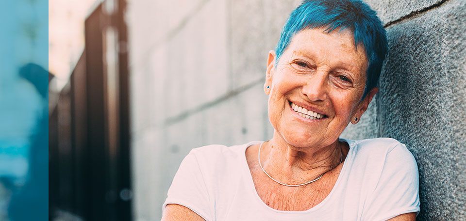A photo of a older women with sharp blue hair leaning against a wall and smiling, taken from Boom Chicka's campaigns for the Free Library of Philadelphia..