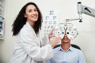 An ophthalmologist is examining a man 's eyes in front of an eye chart.