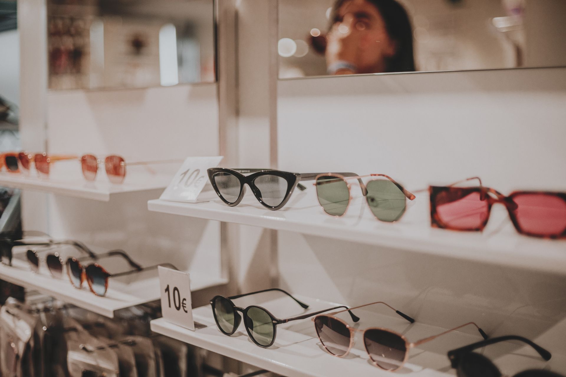 A woman is looking at sunglasses on a shelf in a store. A woman is looking at sunglasses on a shelf in a store.