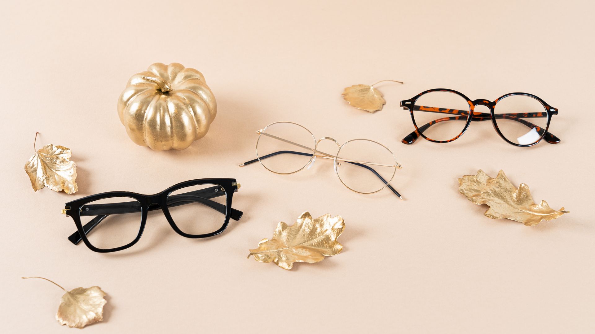 A pair of glasses sitting on top of a table next to a pumpkin and leaves. A pair of glasses sitting on top of a table next to a pumpkin and leaves.