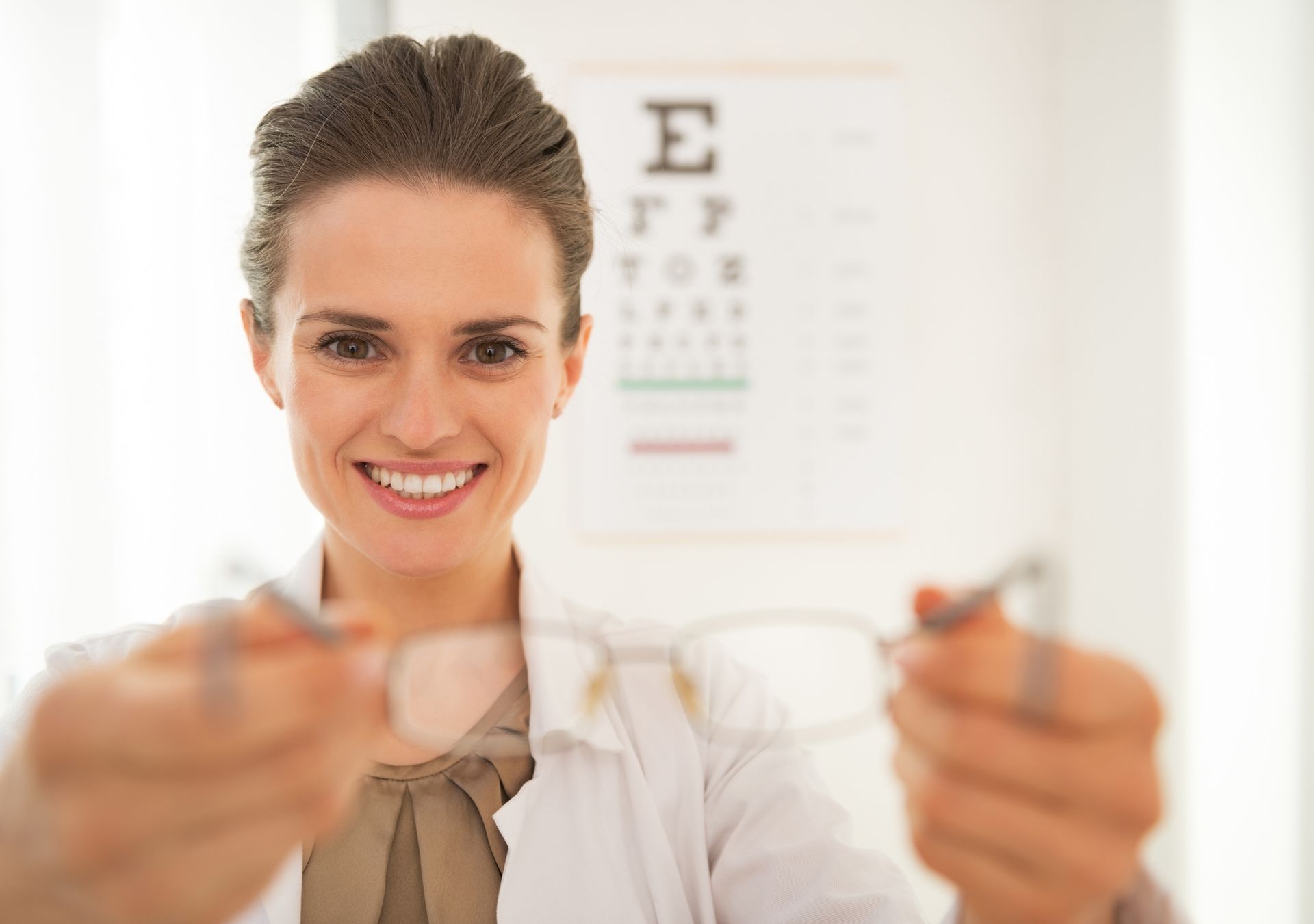 A woman is holding a pair of glasses in front of an eye chart. A woman is holding a pair of glasses in front of an eye chart.
