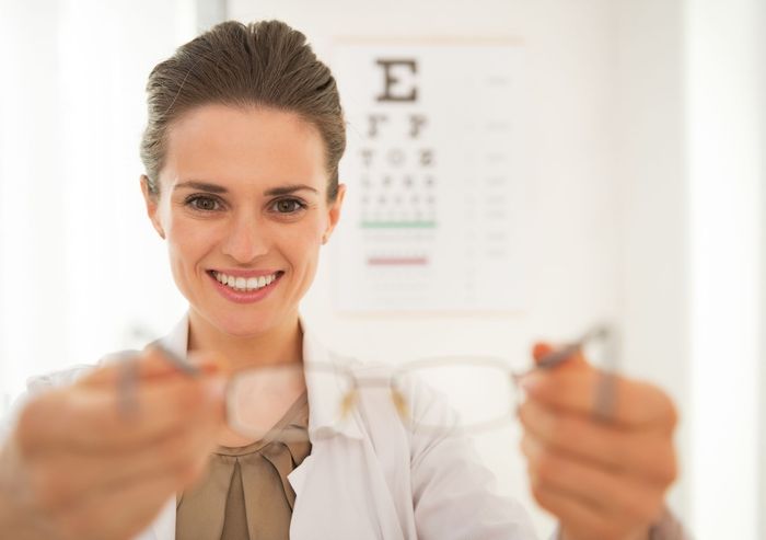 A woman is holding a pair of glasses in front of an eye chart. A woman is holding a pair of glasses in front of an eye chart.