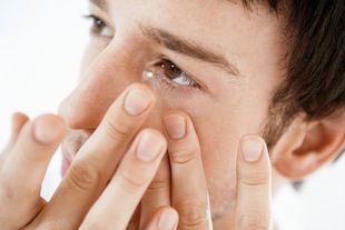 A man is putting a contact lens in his eye.