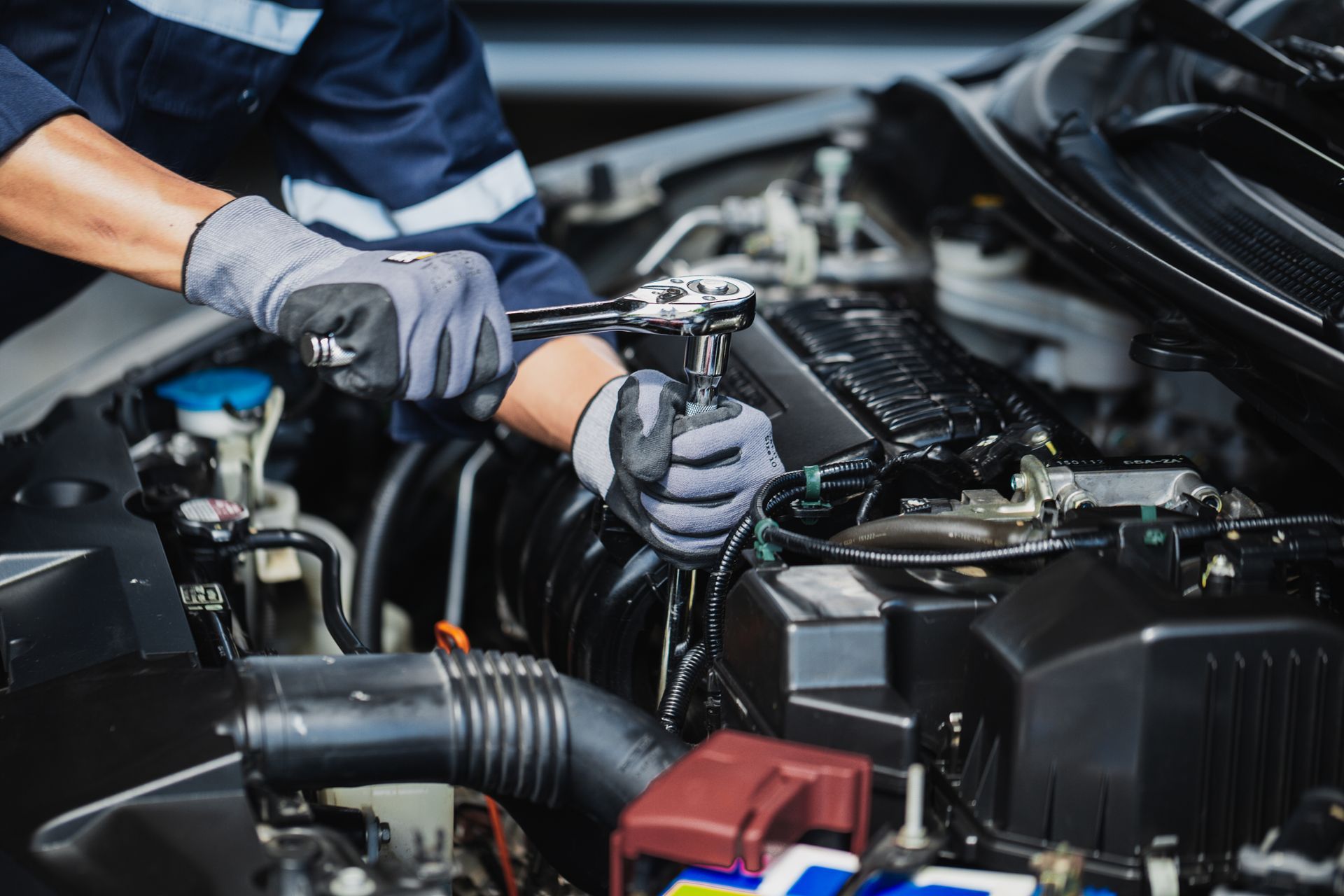 A mechanic wearing gloves performing auto transmission repair on a car engine in a garage.