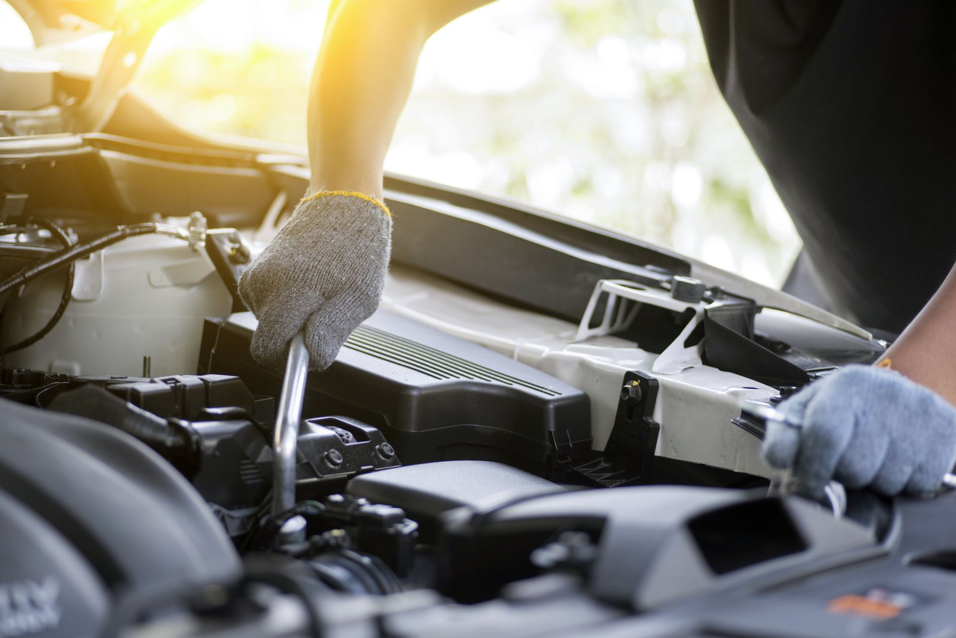 Gloved hands use wrench to repair car engine in daylight setting.