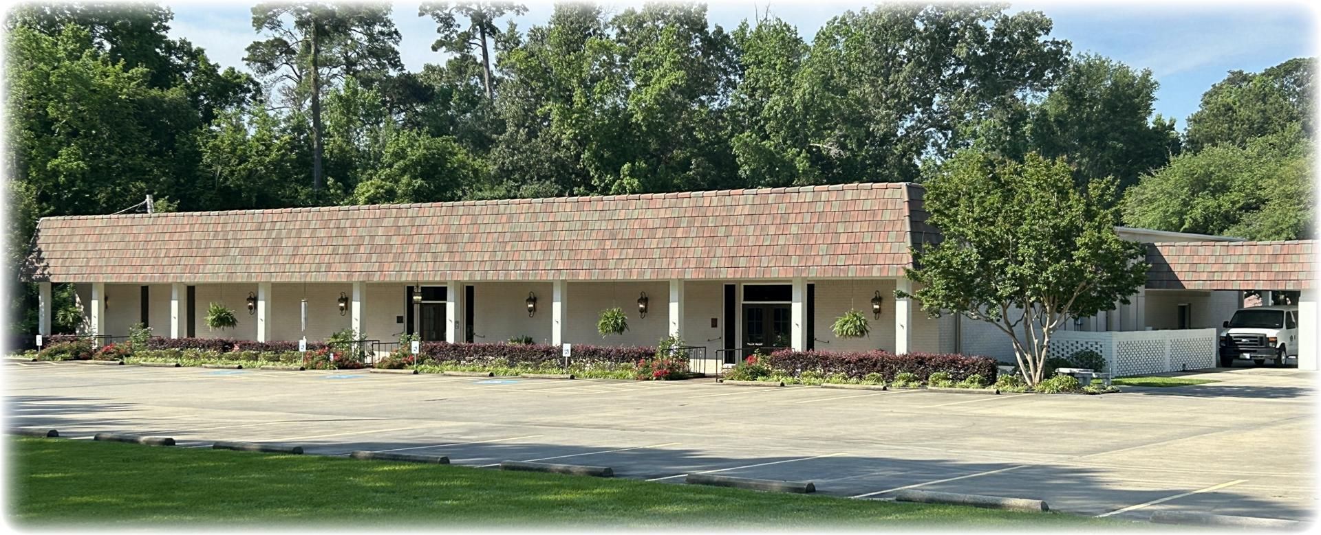 A one-story building with a light-colored exterior and brown roof, surrounded by trees.