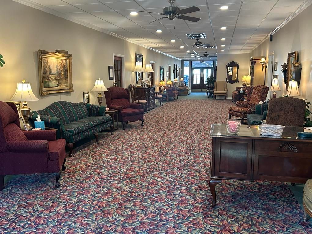 Interior of a long room with chairs, sofas, lamps, and a patterned carpet.