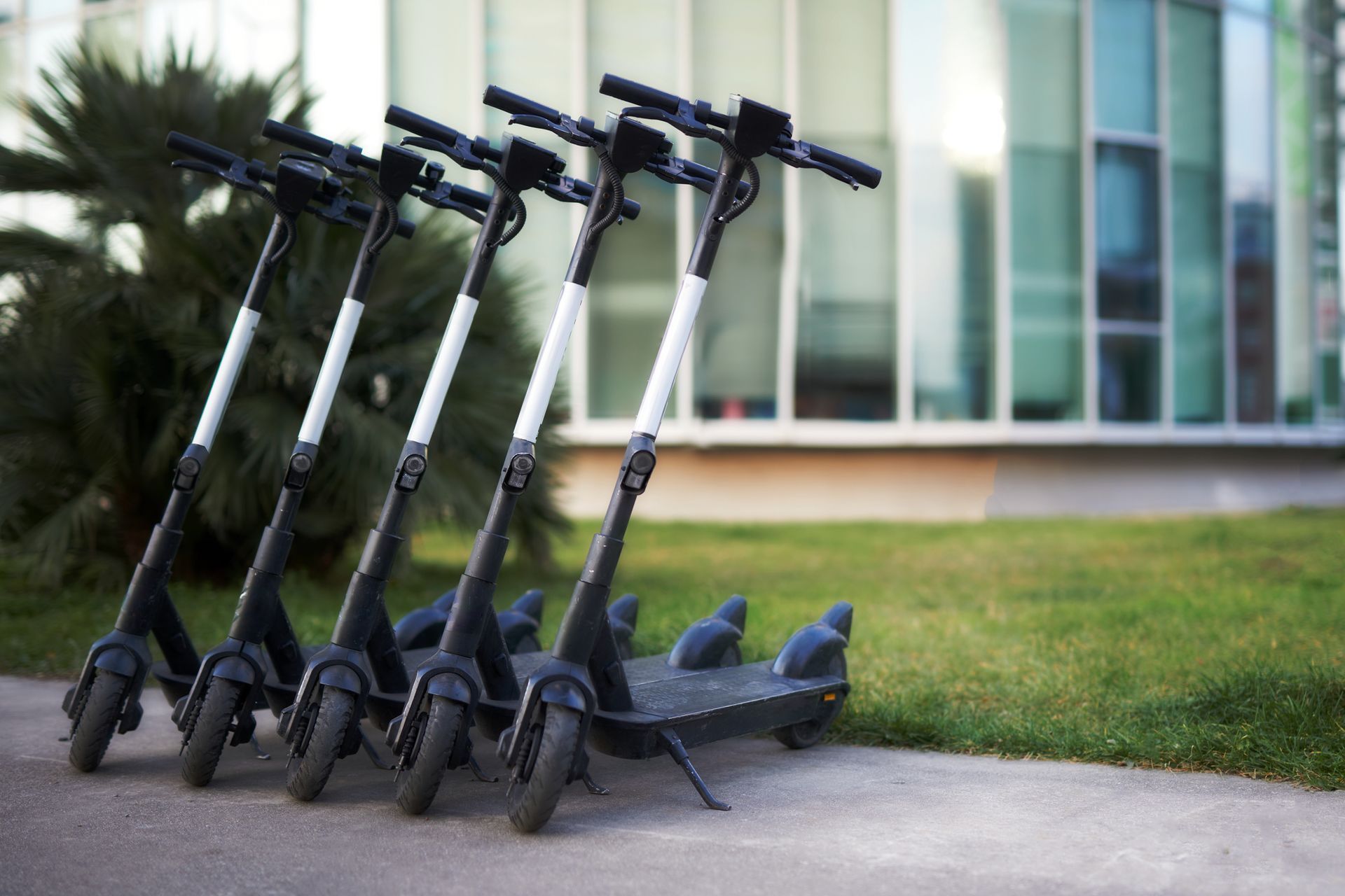 Row of electric scooters parked on a sidewalk near a modern building.