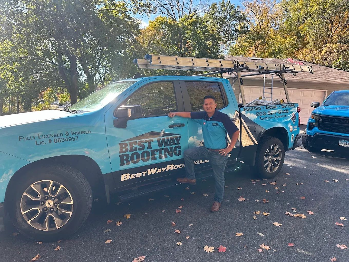 A person stands next to a light blue Best Way Roofing truck with a ladder on top.