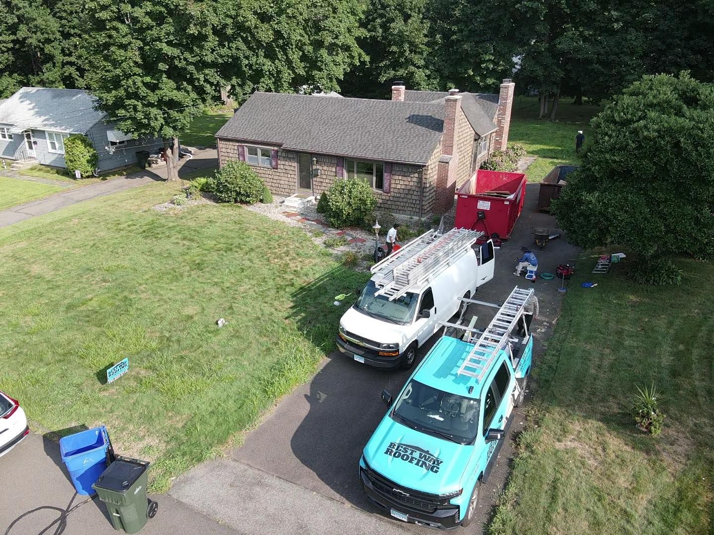 Aerial view of a house with two vans and a dumpster in the driveway, suggesting a renovation or repair project.