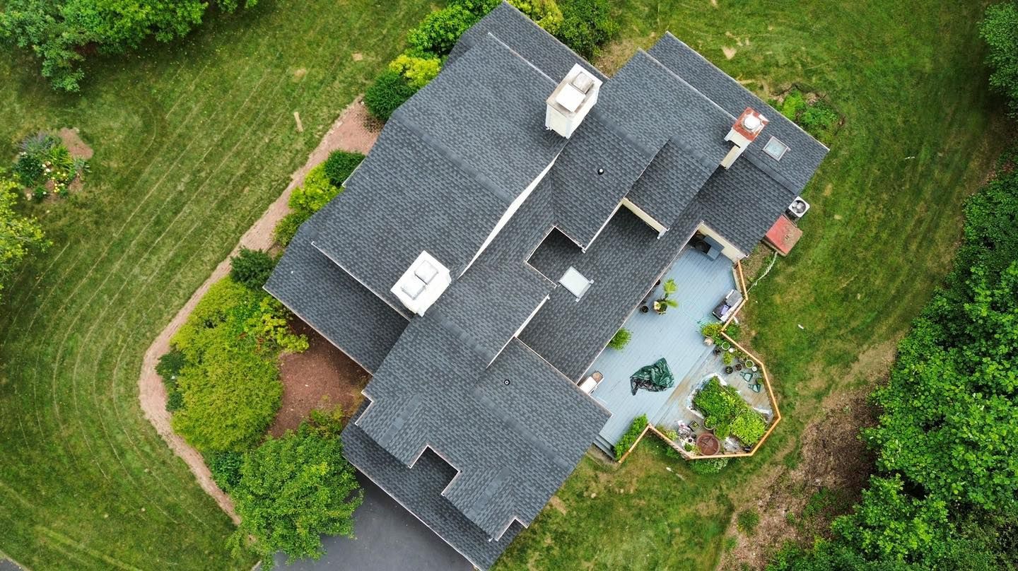 Aerial view of a gray-roofed house with a blue patio, surrounded by green grass and trees.