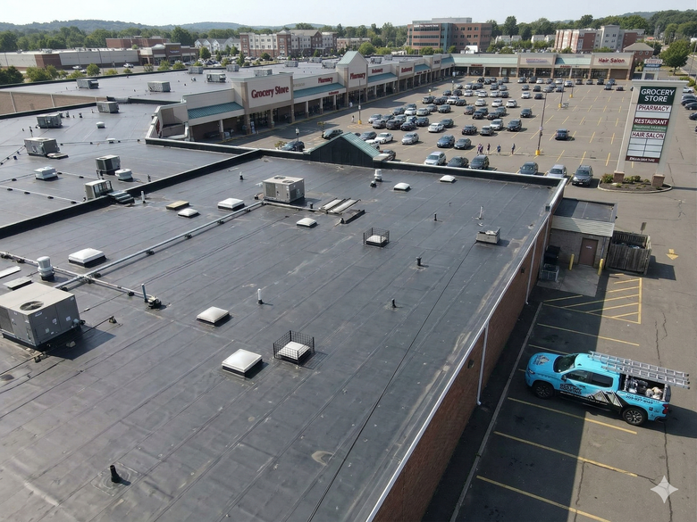Two people working on a gray metal roof, possibly installing solar panels; aerial view.